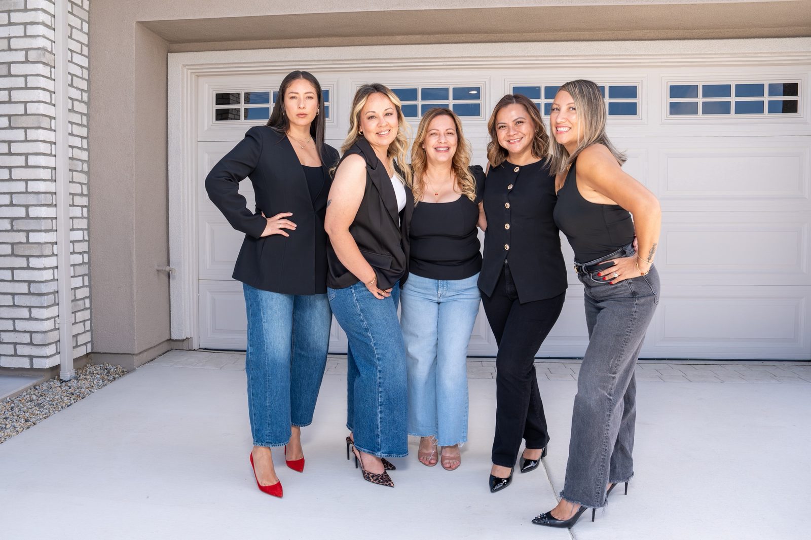 Jenn and four fellow agents smiling together in front of a home's garage